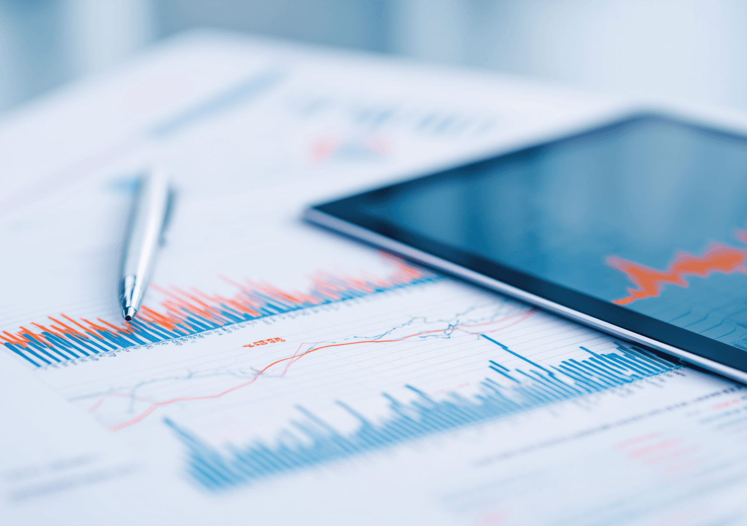 Printed financial charts, a pen and a tablet on a desk