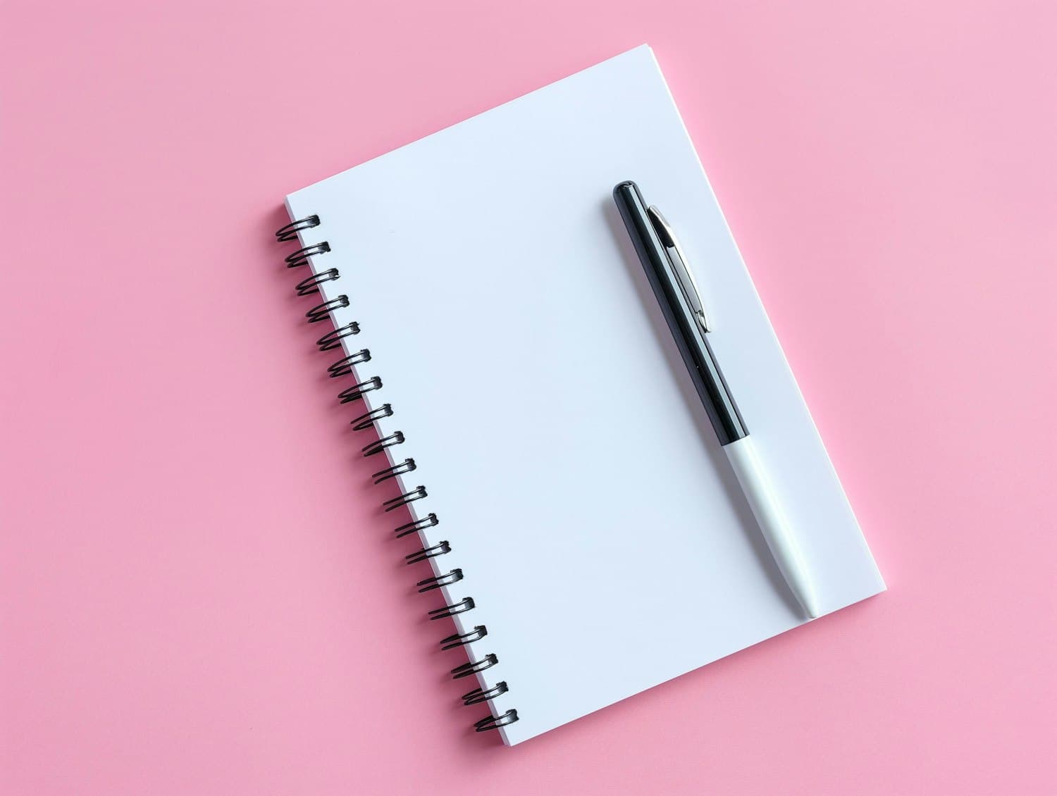 A spiral notebook and pen arranged on a soft pink background