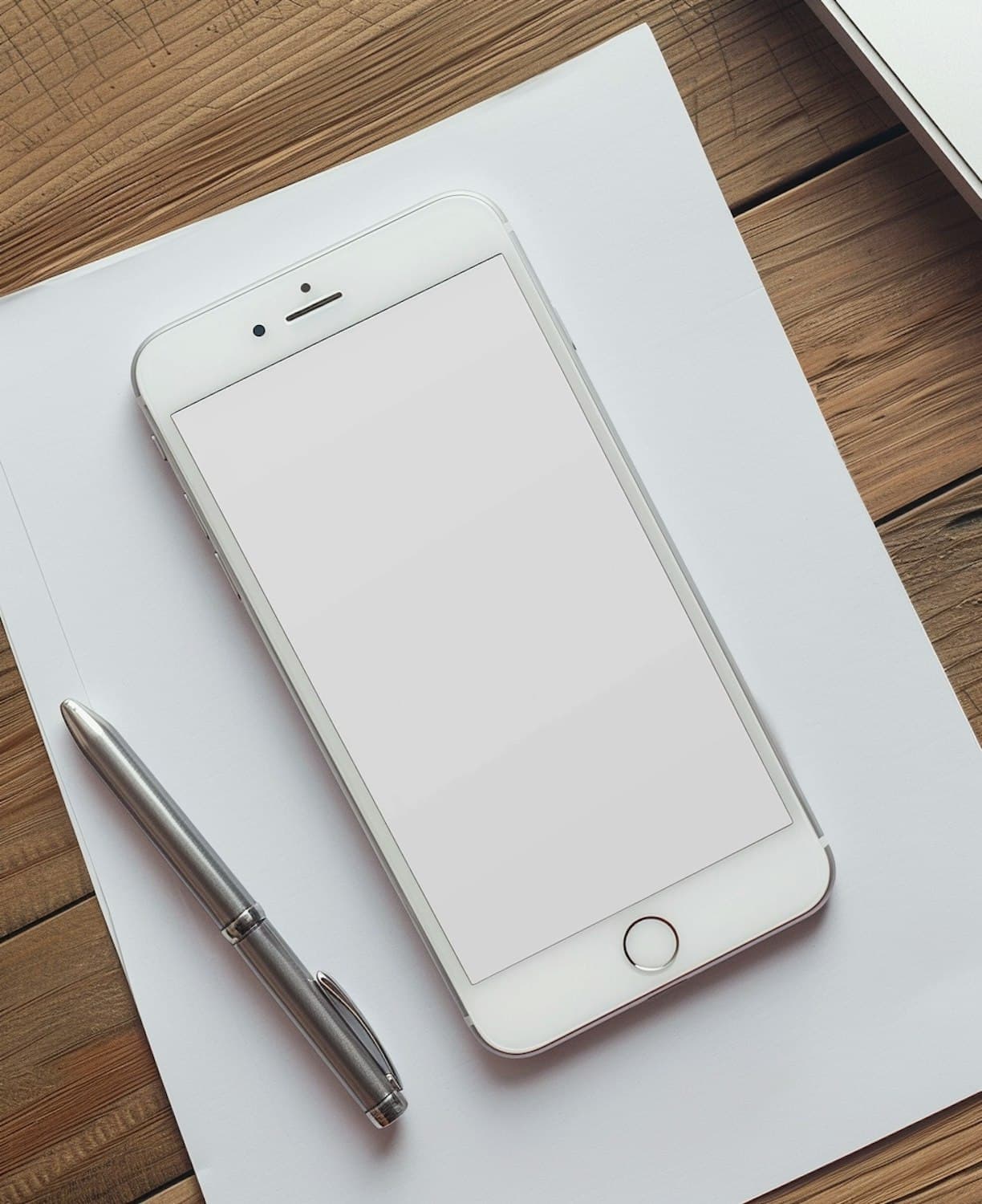 A phone, pen and paper laid out on a wooden desk